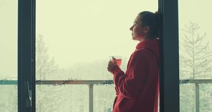 Woman drinks tea, and relax on terrace at home in winter day. Health care, authenticity, sense of balance and calmness. Fresh air, It's Snow time. 4K Video