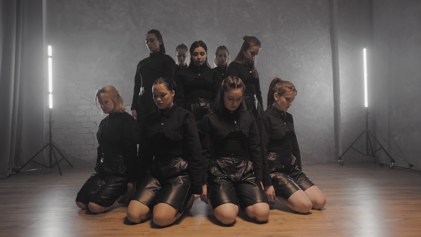 A group of beautiful girls dancing indoors in black suits. Dances