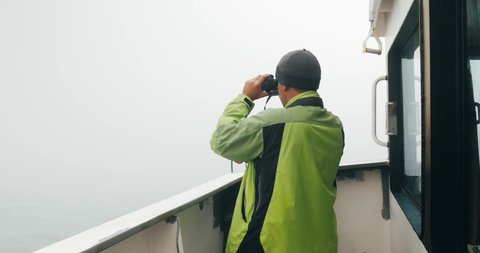 Yuzhno-Sakhalinsk, Russia - August 10, 2015: The watch on duty of the merchant ship looks through binoculars on the outer bridge of the ship.