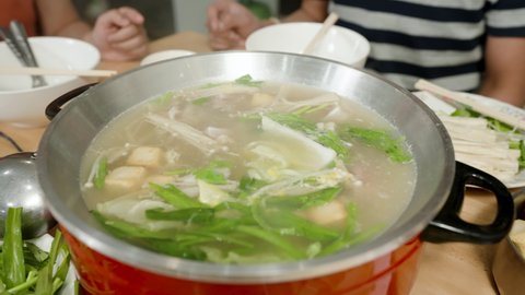 4K, The red sukiyaki pot had boiling water and the hand was putting vegetables and meat into the pot to prepare to eat.