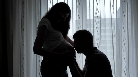 Husband Kisses Pregnant Wife Tummy Silhouette Against Window Background