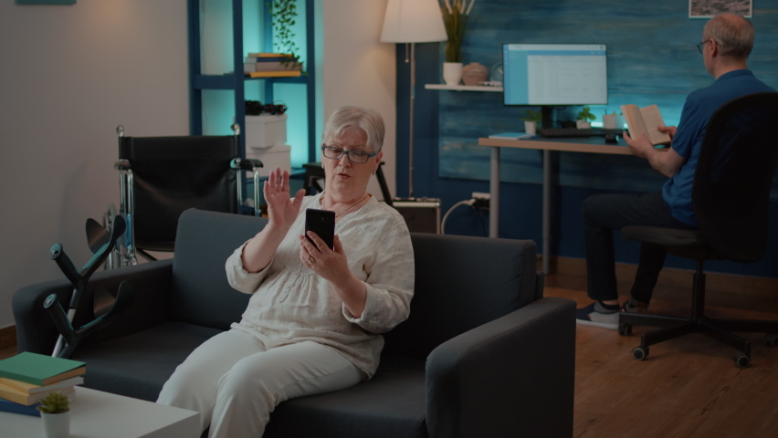 Senior woman waving at video call webcam on smartphone, talking to family on online videoconference. Elder adult using remote conference and telecommunication to chat on mobile phone. Royalty-Free Stock Footage #1085297594