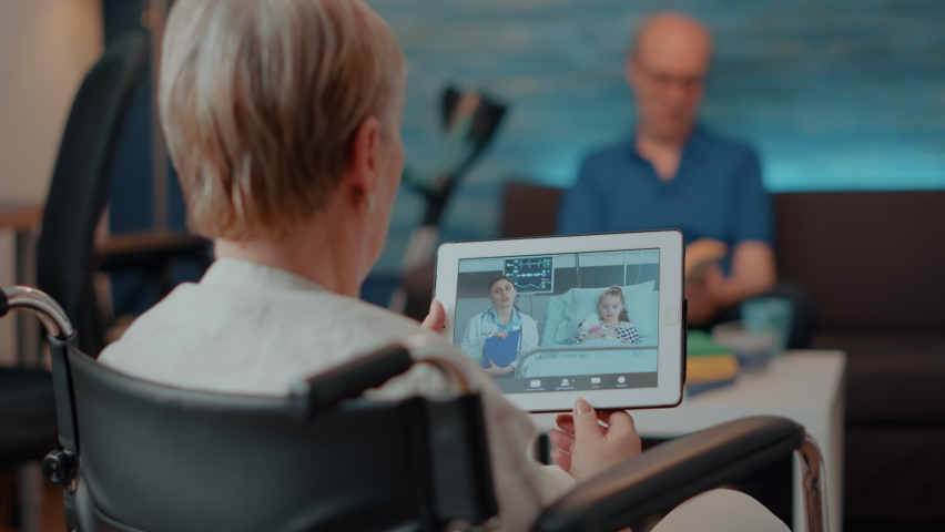 Elderly person holding digital tablet with remote videocall, sitting in wheelchair. Older woman with disability talking to doctor and niece on online teleconference chat, using device. Royalty-Free Stock Footage #1085297762