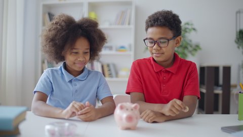 Brother and sister putting coins into piggybank, saving money for their dream