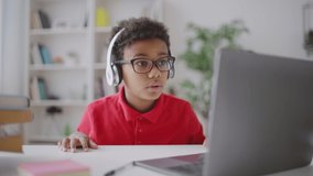 Joyful kid in headphones talking to friend online, using laptop application