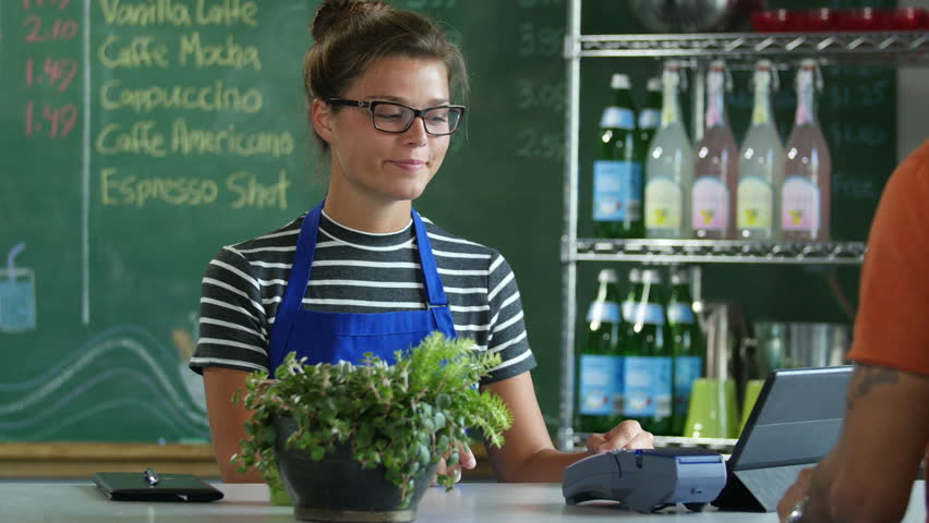 A cashier taking payment from a customer using a credit/debit card in a cafe setting