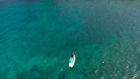 Drone shot, young woman on a paddle board rowing on turquoise water. She stands on paddle board and enjoys relaxation on tropical turquoise lagoon