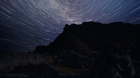 Mesmerizing timelapse of the star trails and northern lights in the dark night sky above the mountains. Parallax video.