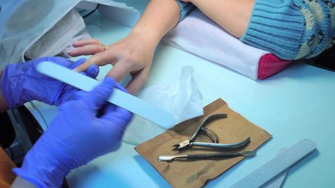 Close-up of a manicure master in blue gloves filing nails with a special nail file, macro. Nail treatment process