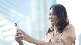 asian woman using smartphone to video call at outdoor space. Happy business woman standing and video calling distance friend online in mobile chat application. Woman checks notification.