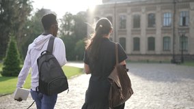 Back view young interracial couple of students walking on sunny morning to university campus outdoors. Confident smart African American man and Caucasian woman strolling talking in sunshine - Powered by Shutterstock - Get 15% off with code: PIKWIZARD15