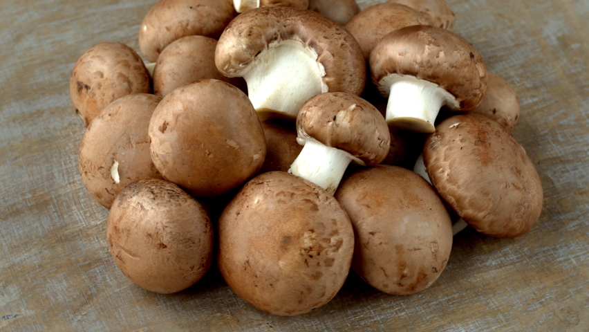 Heap of Champignon mushrooms. Brown edible fungi pile on a wooden table. Table rotate. | Shutterstock HD Video #1085314028