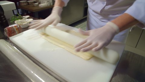 Closeup cook hands rolling dough with rolling pin on kitchen board. chief preparing dough at restaurant. gloved hands cooking, making thin dough sheet with rolling pin. professional food preparation