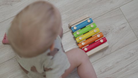 Cute little child sitting on the floor playing with colorful wooden xylophone musical toy for kids, 10 month old baby boy at home. Musical instruments for children to learn to play music.