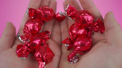 hands holding chocolates in red wrapper, pink background.