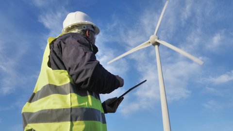 wind technician worker using tablet under wind turbine power plant genarator in the background,low angle shot
