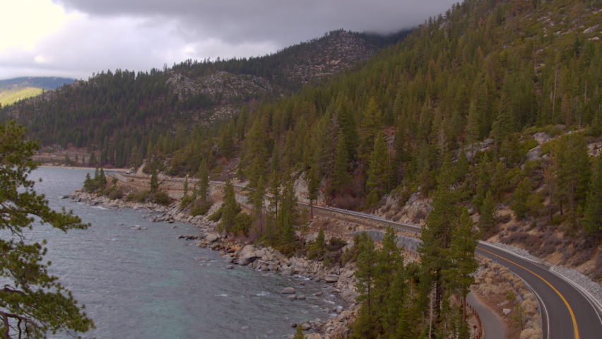 Aerial of road winding around Lake Tahoe in Nevada on a pretty winter day with a Douglas Fir tree in the foreground.