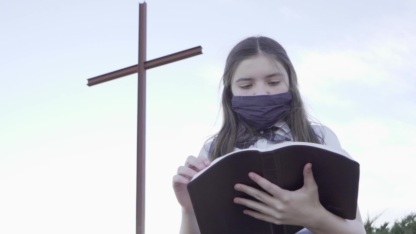 Young teenage school girl in uniform reading the Bible with large cross and sunshine behind her. Growing stronger in Jesus through reading the Word Of God, the Holy Bible. 