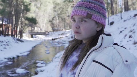 Young attractive depressed teenage girl looks upon nature for peace and hope. Nature's mountain snow filled landscape and streams provides a beautiful winter wonderland in New Mexican mountains.