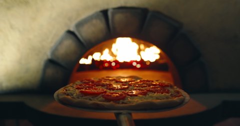 POV bakery worker putting Italian pizza with tomatos in stone oven with peel. Point of view of cooking pizza with traditional recipe - food and drink close up 4k footage