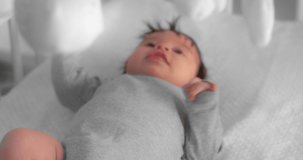 Newborn baby in a gray bodysuit is lying in a crib and looking at a child mobile. Neonate toddler in a nursery room. High quality 4k video. Shot with RED camera.