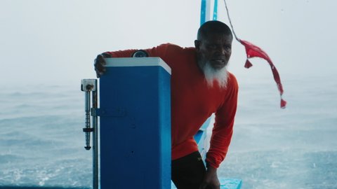 Portrait of the boat captain in Maldives. Maldivian senior man with white beard steers the boat in a harsh weather conditions with strong wind waves and rain shower