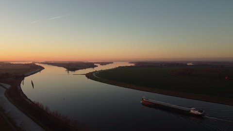 Aaerial view on a ship sailing on the river Ijssel during sunrset during a cold winter afternoon in Overijssel, Netherlands.