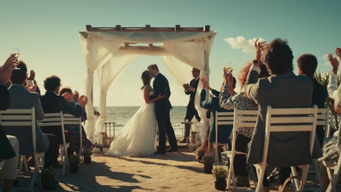 Beautiful Bride and Groom During an Outdoors Wedding Ceremony on an Ocean Beach. Perfect Venue for Romantic Couple to Get Married, Exchange Rings, Kiss and Share Celebrations with Multiethnic Friends.