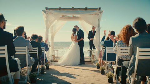 Beautiful Bride and Groom During an Outdoors Wedding Ceremony on a Beach Near the Ocean. Perfect Venue for Romantic Couple to Get Married, Kiss and for Friends with Multiethnic Cultures to Celebrate.