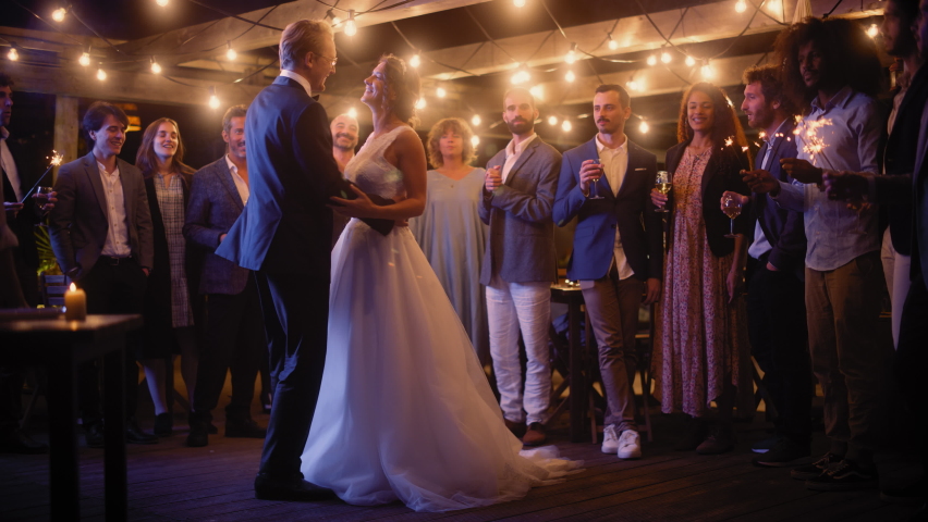Beautiful Bride in White Dress and Groom in Stylish Black Suit Celebrate Wedding at an Evening Reception Party. Newlyweds Dancing at a Venue with Best Multiethnic Diverse Friends. Royalty-Free Stock Footage #1085341094