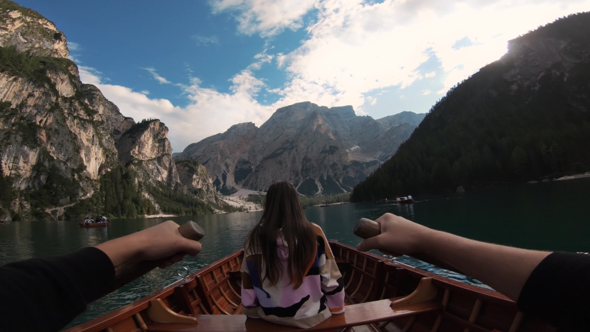Young woman sitting on the edge of a wooden boat in Lake Braies, Dolomites. Tourist girl enjoys the  alpine azure lake clear water fabulous nature of mountain green forest Italian Alps Royalty-Free Stock Footage #1085347025