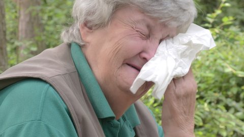 Closeup shot of an elderly caucasian lady laughing. Drying her eyes with a napkin. Fun and joy. Green nature in the background. Grey hair. Humor and jokes. Pensioner.