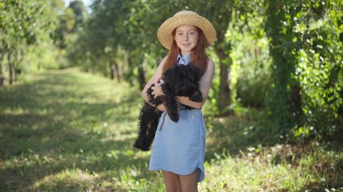 Happy teenage girl posing with black Norfolk Terrier in summer spring park on sunny day. portrait of Caucasian redhead teenager and charming pet enjoying leisure outdoors