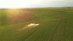 Aerial footage of an agricultural tractor spraying soybean field herbicides at sunset. Location place agrarian region Ukraine, Europe. Cinematic drone shot. Filmed in UHD 4k video. Beauty earth.