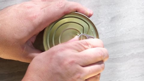 Opening a tin can with red caviar. Male hands open a tin can with salmon caviar on the kitchen table.