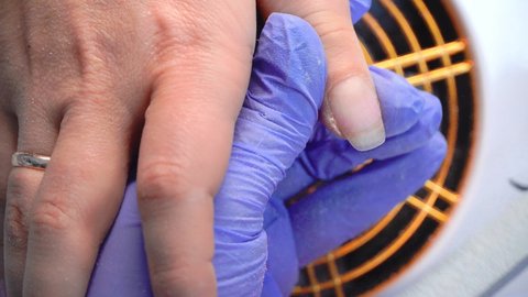 Close-up of a manicure master in blue gloves filing nails with a special nail file. Nail treatment process.