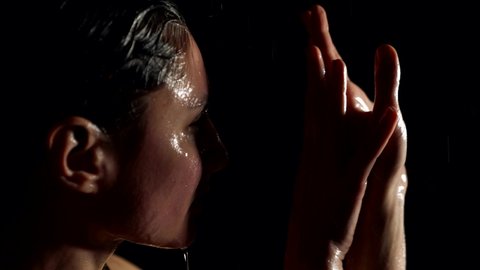emotional woman in shower or rain, playing with light sensually, water is flowing over face