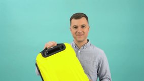 A Caucasian middle-aged man in a blue shirt expresses delight and joy with a yellow suitcase in his hands. An office worker is preparing for a vacation or business trip