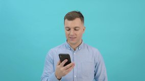 Caucasian middle-aged man in a blue shirt raises a smartphone to his ear and talks. Office worker having a phone conversation in front of a bright blue background