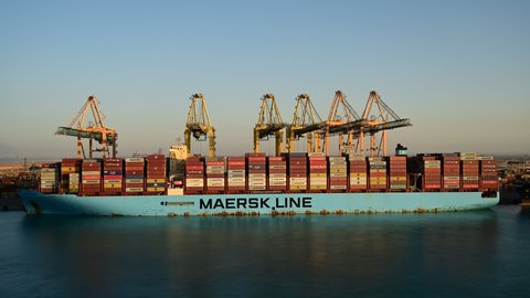 Jeddah, Saudi Arabia – January 9th, 2022: Time-lapse container ship in export and import business and logistics. Container cargo freight ship with working crane bridge at Jeddah international port.