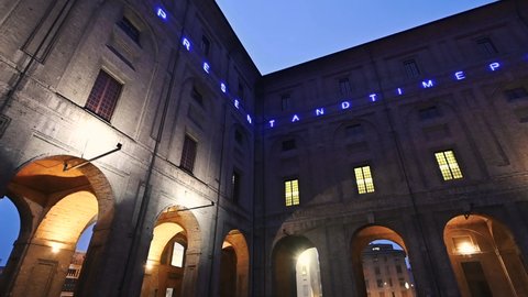 Parma, Emilia-Romagna, Italy.January 2022. Pan nocturnal footage in the courtyard of Palazzo della Pilotta, a luminous writing runs along the entire facade. A small group of tourists.