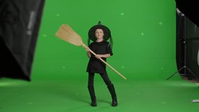 Happy smiling caucasian girl wearing witch hat for halloween parties over green screen background. The child dancing with broom . Halloween concepte. Chroma key. 4k uhd video