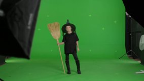 Happy smiling caucasian girl wearing witch hat for halloween parties holding broom over green screen background. Halloween concepte. Chroma key. 4k uhd video