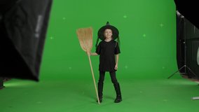 Happy smiling caucasian girl wearing witch hat for halloween parties holding broom over green screen background. Halloween concepte. Chroma key. 4k uhd video