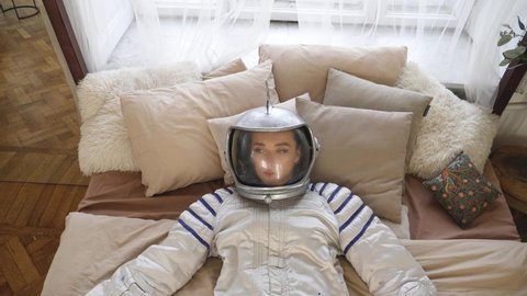 a girl in a space suit and a helmet, lies on the bed and looks up, moves her hands from side to side, simulating an object in weightlessness
