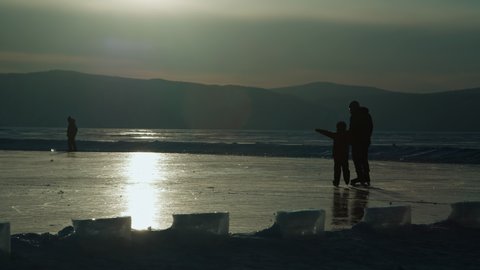 Father and son go ice skating on a frozen lake at sunset in winter