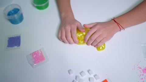 girls hand playing with yellow shiny slime at the table at home