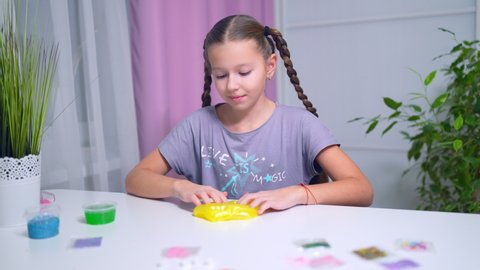 teen girl playing with green shiny slime at the table at home