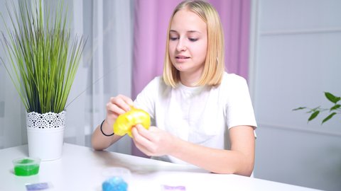 girl playing with yellow shiny slime at the table at home