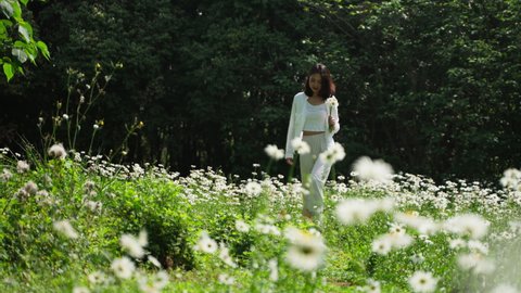 Slow motion of pretty young asian woman in white shirt holding bunch of flowers walking in the blooming field enjoy the beautiful spring day